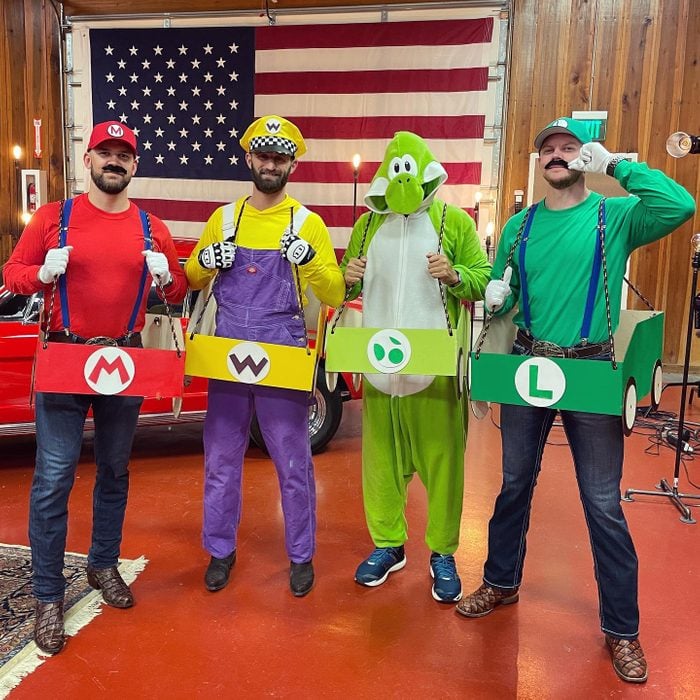 Four men are dressed up as characters from Mario Kart. They are wearing red, yellow, and green and have boxes around them that are meant to be their carts. 