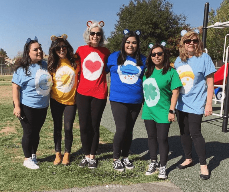 Six women are dressed up in different colored shirts with different symbols on them. They are all wearing bear ears.